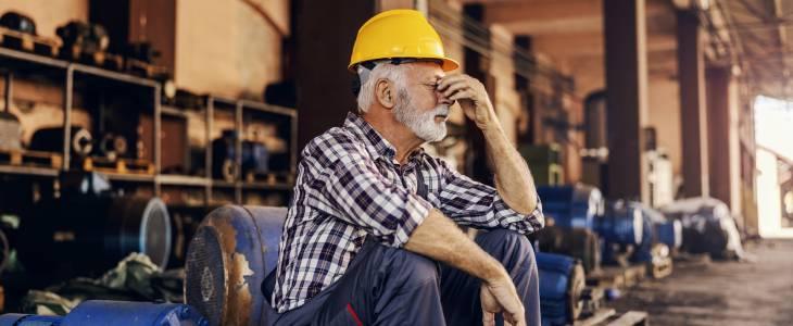 Old blue collar worker sitting and rubbing forehead