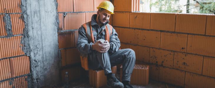 Construction worker holding injured knee in pain.