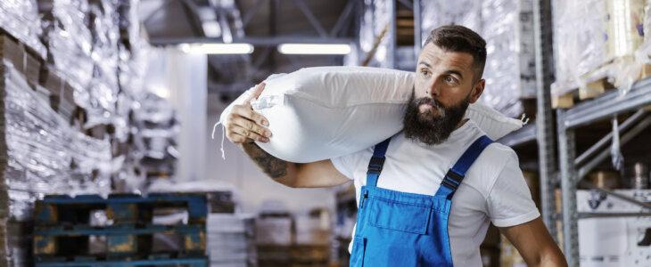 warehouse worker is holding a sack with flour on his shoulder
