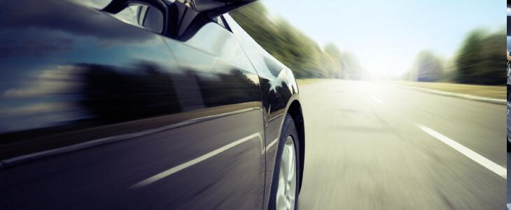 Sleek car driving fast on a sunny road.